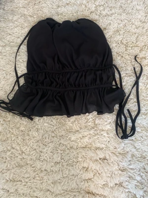 Svart croppad linnetopp med snörning - Trendig svart croppad linnetopp med snörning i sidorna och volangkant nedtill. 