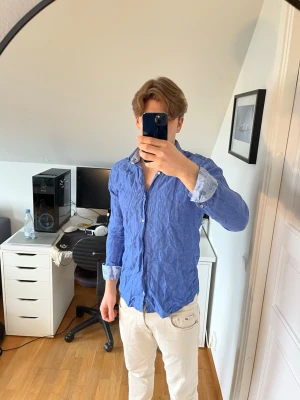 Blå linneskjorta från Riley - Säljer en snygg blå skjorta från Riley i 100% linne. Skjortan har klassisk krage och vita knappar. Det följer även med 3 extra knappar. Hör gärna av dig vid frågor!