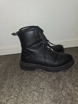 Svarta snörade stövletter - Tuffa svarta stövletter i skinnimitation med grov sula och snörning framtill. Skorna har dragflik bak och detaljerade sömmar. Perfekta för dig som gillar en edgy stil och vill ha något som funkar till många outfits. Storlek EU 41/UK 7
