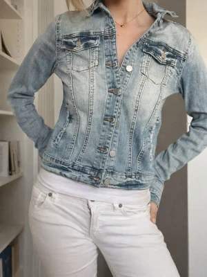 Ljusblå klassisk jeansjacka - Säljer en ljusblå jeansjacka med snygg tvätt och silverfärgade knappar. Figurnär passform och klassisk krage. Perfekt att slänga över en t-shirt för en avslappnad look. 