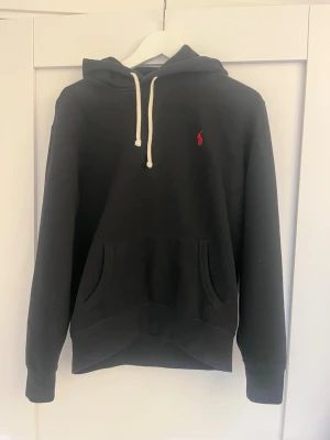 Svart Ralph Lauren Hoodie - Svart Ralph lauren hoodie som är väldigt eftertraktad och populär. Skicket är bra och inga defekter som helst, endast lite luddig men väldigt enkelt att få bort. Nypris: Ca 2000kr. Hör av dig vid frågor!😁