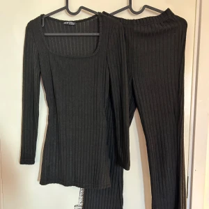 Svart ribbat 2-delat set från SHEIN - Svart ribbad tröja och byxa från SHEIN i storlek 34. Tröjan har en fyrkantig halsringning och långa ärmar med slits på båda sidorna och byxorna är ribbade. Aldrig använda.
