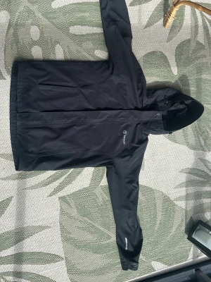 Svart regnjacka från Tenson - Snygg svart regnjacka från Tenson med huva och dragkedja framtill. Jackan har minimalistisk design, diskret logga på bröstet och justerbar huva. Perfekt för regniga dagar och enkel att matcha med olika outfits. Tillverkad i vattenavvisande material.