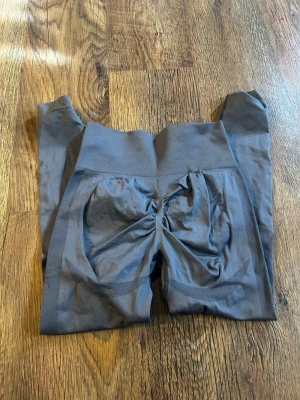 Grå scrunch leggings med hög midja - Säljer ett par grå leggings med scrunch-detalj bak och hög midja. De är sömlösa och har en tight passform som framhäver formerna. Perfekta för gymmet eller till vardagslooken. Materialet känns stretchigt och bekvämt.