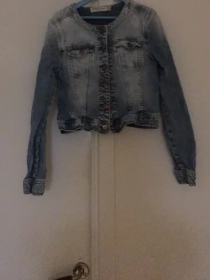 Ljusblå croppad jeansjacka - Säljer en ljusblå croppad jeansjacka med klassisk knappstängning framtill och två bröstfickor. Jackan har långa ärmar och en snygg denimlook som ger en avslappnad vibe. Perfekt för kalla sommardagar!💕OBS! Den är i storlek 158 men den känns mindre som ungefär 146/152!💗