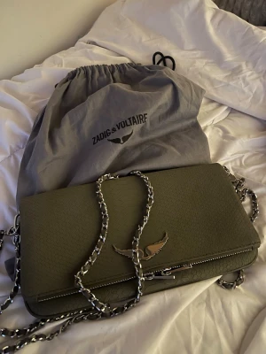 Olivgrön axelväska Zadig & Voltaire - Snygg olivgrön axelväska från Zadig & Voltaire i strukturerat läder. Väskan har en silverfärgad kedjerem och ikonisk metallvinge på framsidan. Perfekt storlek för det viktigaste och levereras med dustbag.