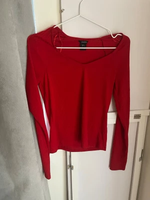 Röd långärmad topp från Lindex - Snygg röd långärmad topp från Lindex med v-ringad halsringning. Modellen är enkel och figurnära med mjukt, stretchigt material som passar perfekt till jeans eller kjol. Klassisk design utan mönster eller extra detaljer.