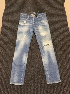 Äkta! Ljusblå slitna jeans från Dsquared2 - Säljer ett par ljusblå jeans från Dsquared2 med trendiga slitningar och färgstänk. Jeansen har rak passform, klassiska fem fickor och knappgylf. Perfekta för dig som gillar en avslappnad och cool streetstil. Pris kan diskuteras!