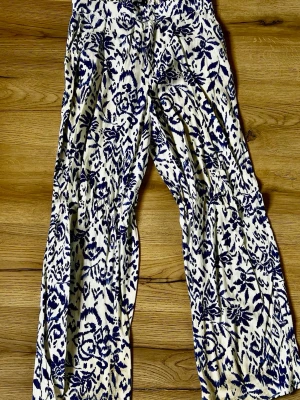 Mönstrade blåvita linnebyxor från Gina Tricot - Säljer ett par luftiga linnebyxor med blått mönster på vit botten. Byxorna har rak passform och resår i midjan för extra komfort. Perfekta för dig som gillar en avslappnad och trendig stil. Botten är lite smutsig men går nog att tvätta