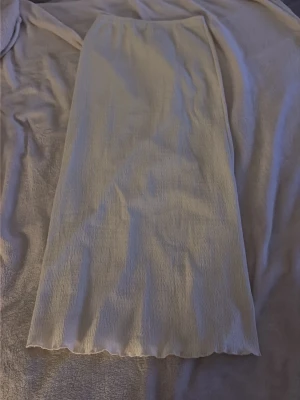 Lång vit kjol i strukturerat tyg - Säljer en lång vit kjol med rak passform och strukturerat tyg. Kjolen har en enkel och stilren design utan synliga detaljer, perfekt att matcha med olika toppar för en clean look.