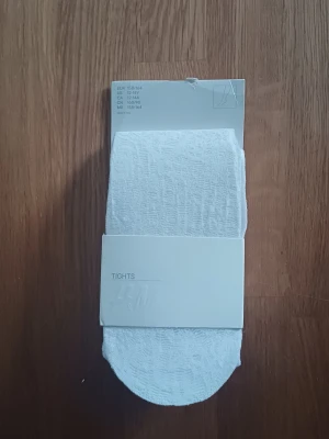 Vita tights från H&M - Säljer ett par vita tights från H&M i storlek 158/164. Tightsen är tunna och stretchiga, perfekta att ha under kjol eller klänning. Materialet är mjukt och bekvämt, och de har en enkel, klassisk design utan synliga mönster.