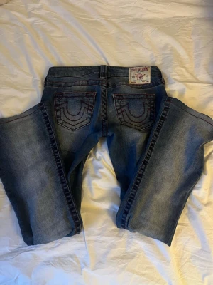 Unika True Religion jeans  - Snygga blå jeans från True Religion med röda sömmar. Jeansen är också redan uppsydda och passar mig som är runt 160cm.