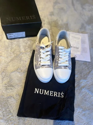 Skor från Numeris - Snygga sneakers från Numeris i grått och vitt med vita snören och sula. Skorna har ett diskret mönster på sidan och logga på hälen. Ovandelen är i textil och syntet, och sulan är i gummi. Perfekta för dig som gillar stilrena och trendiga sneakers. Kvitto finns!  Pris kan diskuteras!