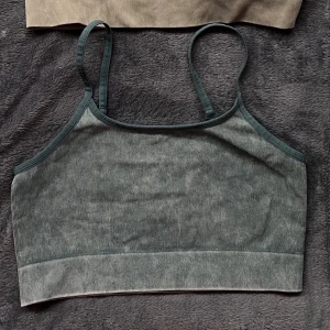 2-pack ribbade crop-toppar - Säljer ett 2-pack ribbade crop-toppar med smala axelband. Ena toppen är mörkgrå och den andra beige, båda i stretchigt material som sitter tajt mot kroppen. Perfekta att bära under skjortor eller som de är för en enkel och clean look.