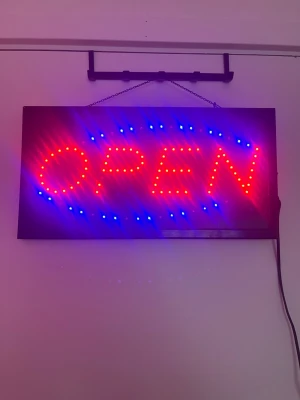 LED, skylt - Elektrisk LED-skylt med texten OPEN i rött och blått ljus. Skylten har en svart rektangulär ram, kedja för upphängning och strömbrytare på sidan. Drivs med sladd och passar perfekt för butik, café eller liknande verksamhet.