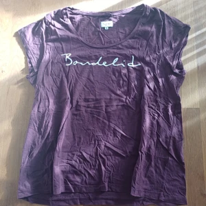 Vinröd t-shirt från Bondelid - Snygg vinröd t-shirt från Bondelid med vitt tryck på bröstet. T-shirten har rund halsringning och korta ärmar. Tillverkad i mjuk bomull som känns skön mot huden. Perfekt för en avslappnad och trendig look.