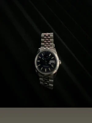 Silverfärgad klocka med länkarmband - Stilren klocka med silverfärgat länkarmband och mörk urtavla. Klockan har markerade index, datumvisning och räfflad bezel. Passar perfekt för dig som gillar klassisk och tidlös design. 