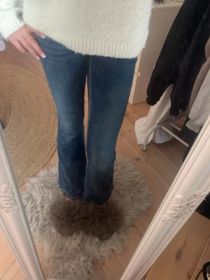 Blå bootcut jeans med kontrastsömmar -  Säljer ett par mörkblå jeans från Gina Tricot i storlek XS. Jeansen har jättefina detaljer på fickorna med paljetter och stenar. Jeansen har en inner benlängd på 80 cm och ett Midjemått rakt över på 38cm. 