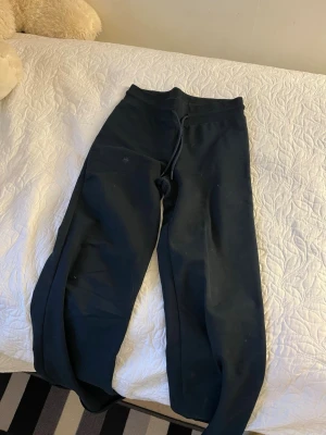 Svarta vida mjukisbyxor med dragsko - Säljer ett par svarta mjukisbyxor med bred passform och dragsko i midjan. Byxorna har raka ben och är tillverkade i ett mjukt och bekvämt material, perfekta för chill dagar. Inga synliga loggor eller märken.