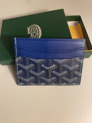 Blå kortfodral från Go4yard - Snyggt blått kortfodral från Go4yard med klassiskt mönster i vitt och mörkblått. Tillverkat i exklusivt läder med flera kortfack. Perfekt för dig som vill ha en stilren och lyxig accessoar i fickan. Levereras med originalask och certifikat.