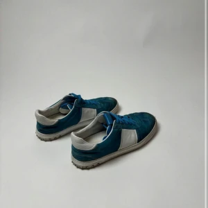 Valentino Flycrew blå - Snygga sneakers i blått och vitt med lågt skaft och klassisk snörning. Ovandelen är i mocka och textil, med vita paneler på sidorna och blå detaljer på tån och snörningen. Mycket fina skor i mycket bra skick.