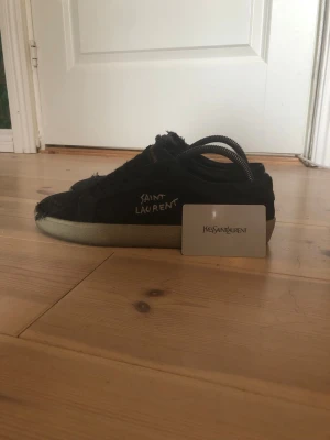Svarta Saint Laurent sneakers - Svarta sneakers från Saint Laurent med slitna detaljer och vit sula. Skon har en låg profil och Saint Laurent-logga på sidan. Tillverkad i tyg och mocka för en cool, avslappnad look. Medföljer originalpåse och kort. Riktigt fina passar perfekt till allt priset är inte hugget i sten och skriv ifall ni har frågor 
