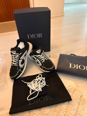 Svarta Dior B30 sneakers - Snygga svarta Dior B30 sneakers med vita detaljer och reflekterande logga på sidan. Skorna har en chunky sula, mesh och mocka-paneler samt vita skosnören. Ikonisk CD-detalj bak på hälen och klassisk Dior-branding på plösen. Perfekta för dig som gillar exklusiva sneakers. Box, påse, dustbag, extra snören med dustbag till dom och en ”bee” logga följer med. Påsen är jätte lite skadad åt sidan. Hör av er om ni har några frågor🤗