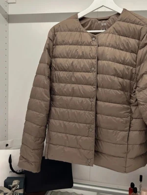Vårjacka Uniqlo - Säljer en beige lättvindsjacka från Uniqlo med rund halsringning och knappar framtill💓 Jackan har en clean och enkel design som passar till det mesta.  OBS, finns en liten fläck vid knapparna på framsidan, se bild 4 😊 har ej försökt tvätta bort den så vet inte om de går