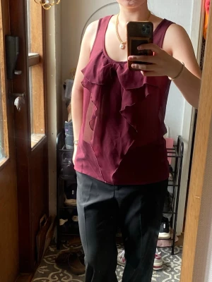 Vinröd linnetopp med volangdetaljer - Snygg vinröd linnetopp med volangdetaljer framtill. Materialet är väldigt genomskinligt och känns lätt och luftigt. Avslappnad passform. 