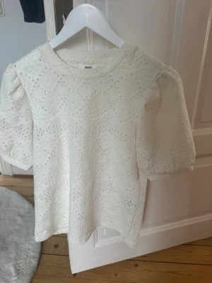 Vit spetsblus från OBJECT - Säljer en söt vit blus från OBJECT med puffärmar och vackert broderad spets. Blusen har rund halsringning och är tillverkad i ett lätt material som känns luftigt. 