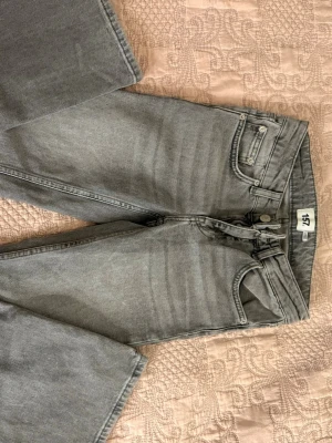 Grå raka jeans från 157 - Säljer ett par grå jeans från 157 med rak passform och klassisk femficksdesign. Jeansen har hög midja, bälteshällor och knappgylf. Materialet är denim i bomull och färgen är en snygg tvättad grå nyans. Perfekta till en avslappnad stil.