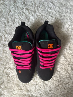 DC Shoes x Desigual sneakers svart rosa - Unika sneakers från DC Shoes i samarbete med Desigual. Svart bas med färgglada detaljer, rosa skosnören och turkosa inslag. Stora broderade Desigual-loggor i rosa, orange och turkos på sidorna. Tjock sula och klassisk låg modell.                            Säljer då de råkade vara lite för små ❤️