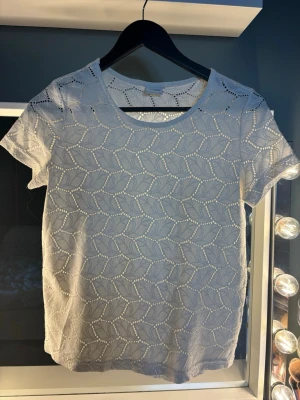 Vit spetsmönstrad t-shirt - Snygg vit t-shirt med korta ärmar och ett genomgående spetsmönster i bladmönster. T-shirten har rund halsringning och är tillverkad i ett lätt och luftigt material, perfekt för varmare dagar. Enkel men ändå unik design som passar till mycket.