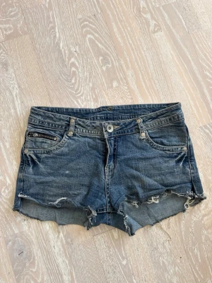 Blå jeansshorts med broderade kronor - Säljer ett par lågmidjade blå jeansshorts från heartquake med råa kanter och slitningar. Köpta från Vinted från början, men inga deffekter finns. Shortsen har en dragkedjedetalj på fickan fram och broderade vita kronor på bakfickorna. Storleken står som 164x, men jag skulle säga att de är i xs/s. För mer bilder eller mått är det bara att skriva. Perfekta för sommaren!