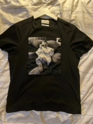 Svart t-shirt från Limitato - Cool svart t-shirt från Limitato med ett stort svartvitt fototryck framtill. T-shirten har rund hals och korta ärmar. Perfekt för dig som vill sticka ut med en unik printad tee.  Storlek m