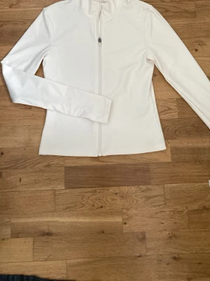 Långärmad träningströja med dragkedja - Tröjan är krämvit och är i ett stretchigt och mjukt material som gör det bekvämt att röra sig. Den är figurnära och har en dragkedja. Tröjan är bara använd en gång och har inga som helst tecken på användning. Skicka gärna prisförslag! 🤗