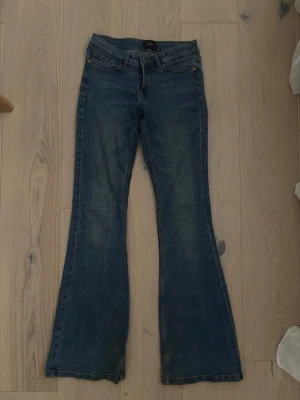 Blå bootcut jeans  - Ett par klassiska blå bootcut jeans från vero moda med fem fickor och lågmidja. Jeansen har lätt slitna detaljer och utsvängda ben, perfekt för en avslappnad och trendig look. Tillverkade i denim med snygg tvätt. Smått slitet längst ner