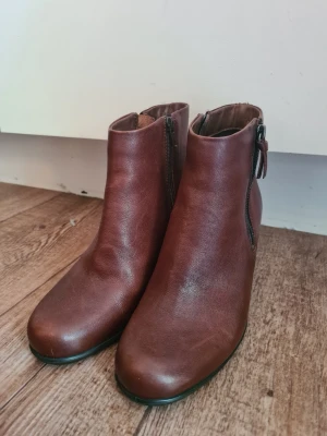 Bruna skinnstövletter Ecco - Bruna stövletter i äkta skinn med rund tå och dragkedja på sidan. Modellen har en stabil, medelhög klack och enkel design utan synliga detaljer. I bra skick med några få märken i storlek 38. Orginalpris 1050 kronor från Ecco. 