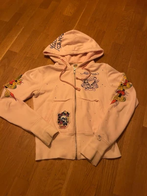 Ljusrosa Ed Hardy hoodie med tryck - Säljer en ljusrosa zip-hoodie från Ed Hardy. Perfekt för dig som gillar streetwear och statement-plagg❤️❤️ Sitter som xs👌👌