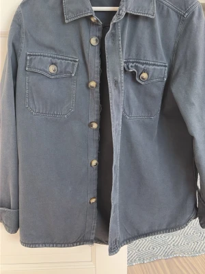 Blå overshirt från Morris - Stilren blå overshirt i denimliknande material med två bröstfickor med lock och knapp. Klassisk krage och knäppning framtill med synliga knappar. Perfekt lager på lager-plagg för en avslappnad look. Ops stor i storleken