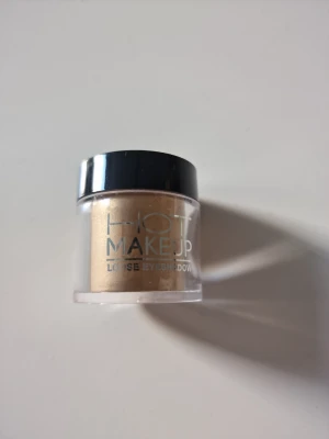 Hot Makeup lösögonskugga guld - Lösögonskugga från Hot Makeup i en snygg guldfärg med skimrande finish. Kommer i en liten rund plastburk med svart lock. Perfekt för föt sommarens festivaler och fester 💛Enkel att applicera och blanda ut för ett kreativt resultat.
