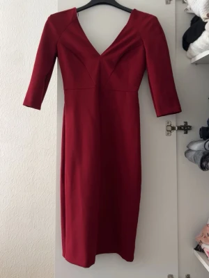 Röd omlottklänning från Dorothy Perkins - Snygg röd klänning från Zara woman med djup V-ringning och trekvartsärmar. Klänningen har figurnära passform och omlottliknande skärning framtill. Tillverkad i ett stretchigt tyg som ger en smickrande siluett.