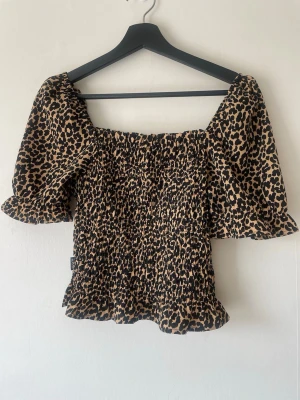 smockad topp med puffärmad leopard - Trendig leopardmönstrad topp från Seaside med puffiga ärmar och smockad kropp. Toppen har fyrkantig ringning och är tillverkad i ett mjukt, stretchigt material som sitter snyggt på kroppen. Perfekt för dig som vill sticka ut med ett djurmönster.