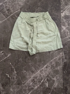 Ljusgröna shorts med knytband - Snygga ljusgröna shorts med hög midja och bred resår samt knytband i midjan. Tillverkade i ett mjukt och lätt material som passar perfekt till varma dagar. Shortsen har en avslappnad passform och sidofickor för extra stilpoäng.