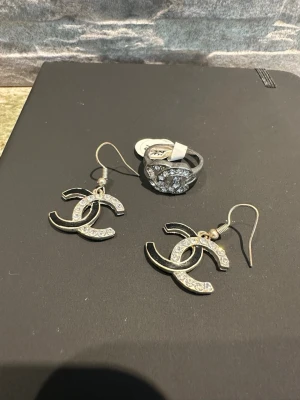 Ett set med  örhängen med stenar och en matchande  ring - ett par C-inspirerade örhängen i silverfärgad metall med gnistrande små stenar och en matchande ring. 