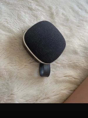 Svart bärbar högtalare med USB - Smidig bärbar högtalare i svart tyg med rundade kanter och en praktisk rem. Utrustad med USB-port, microSD-kortplats och laddningsport. Perfekt för att ta med sig musiken överallt. Modern design med metallram och robust plast på baksidan.
