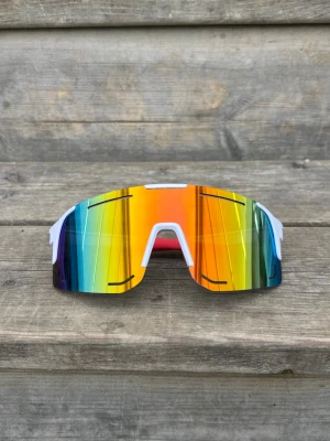 Futuristiska sportiga solglasögon - Säljer ett par riktigt futuristiska solglasögon med spegelglas i regnbågsfärger och vit båge. Glasen har en bred, böjd form som täcker bra och ger en cool look. Perfekta för dig som vill sticka ut och gillar sportig stil.