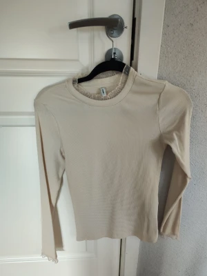 Beige ribbad långärmad topp - Säljer en beige ribbad långärmad topp med rund hals. Toppen har en slim passform och är tillverkad i ett mjukt, stretchigt material som sitter snyggt på kroppen. Perfekt att styla med jeans eller kjol. Den har aldrig använts utan bara blivit testad.