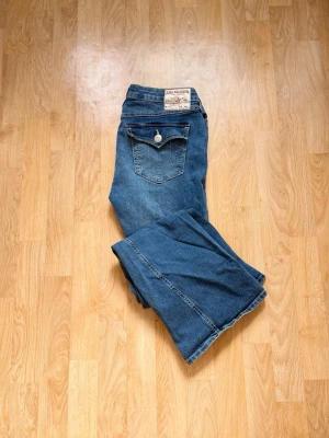 True Religion jeans mid rise flare W31 - Säljer ett par mid rise flare jeans W31(passar large) från True Religion med ikoniska ficklock och vita knappar bak. Jeansen har en snygg tvätt och är tillverkade i slitstark denim. Perfekt för dig som vill ha ett par jeans med unik detalj på fickorna.