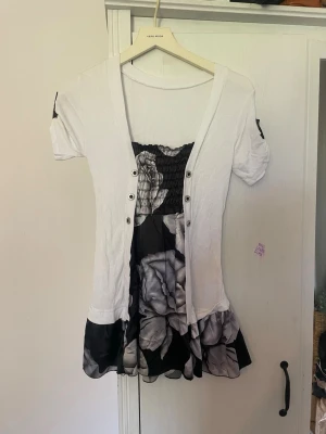 Vintage miniklänning❤️ - Kortklänning med vit överdel och svart kjol med stora blommor i gråskala. Klänningen har korta ärmar, knappar framtill och smock upptill. Kjolen har volangkant och plagget har en feminin, figurnära passform.